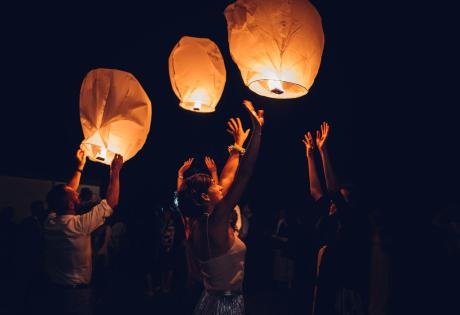 Persone che lanciano lanterne di carta illuminate nel cielo notturno.