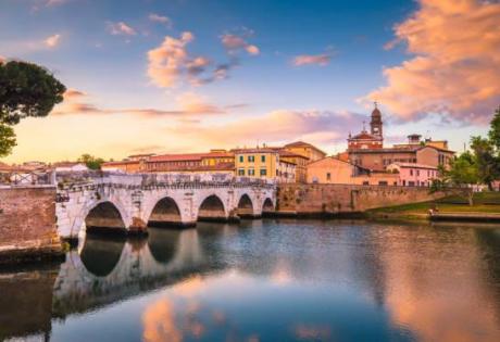 Ponte antico riflesso nel fiume al tramonto, cielo colorato.