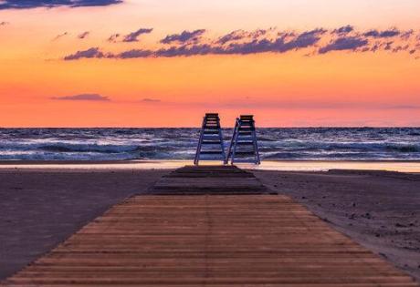 Tramonto sulla spiaggia con passerella e sedie a sdraio.