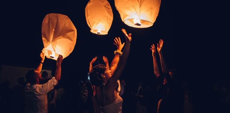 Persone che lanciano lanterne di carta illuminate nel cielo notturno.