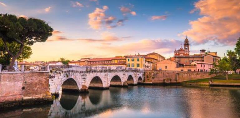 Ponte antico riflesso nel fiume al tramonto, cielo colorato.